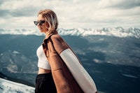 a woman standing on top of a mountain wearing sunglasses and a brown coat